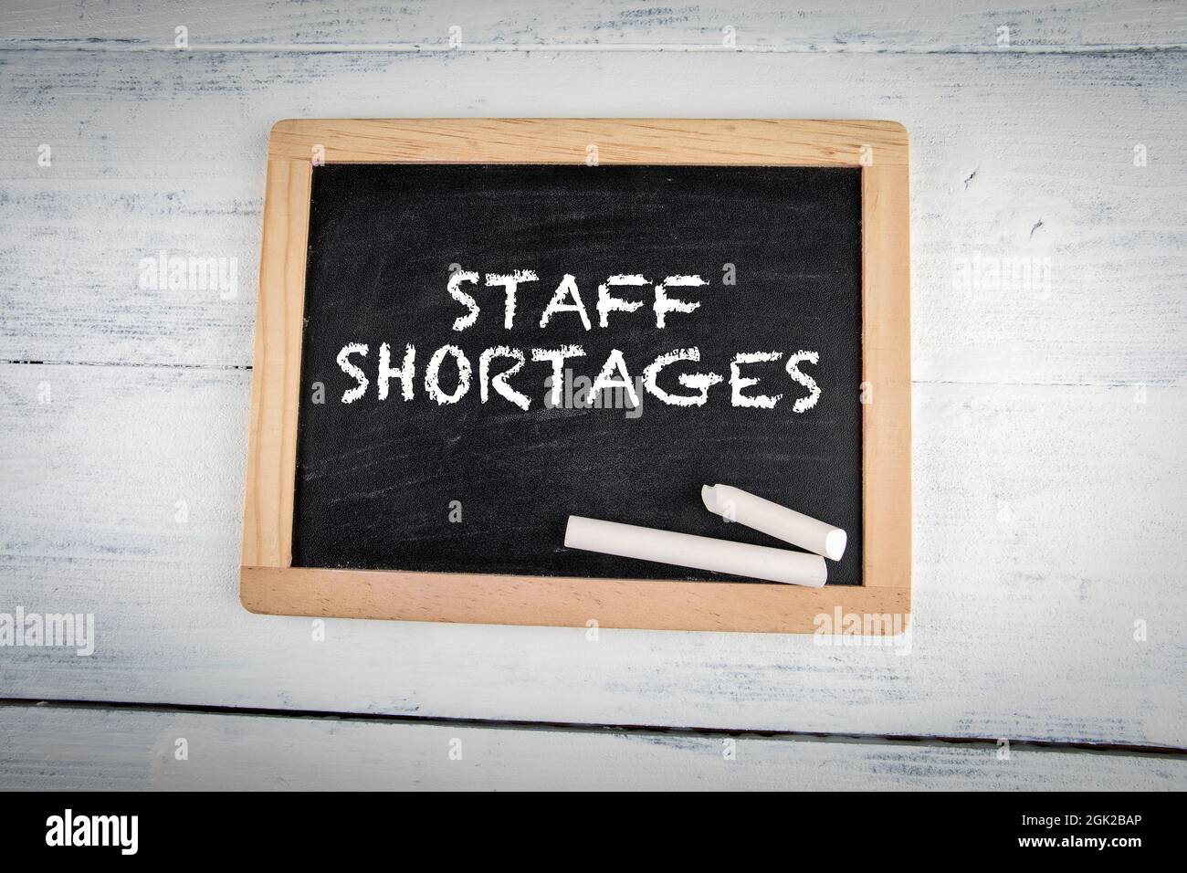 Staff Shortages. Chalk board with white pieces of chalk on a wooden table. Stock Photo