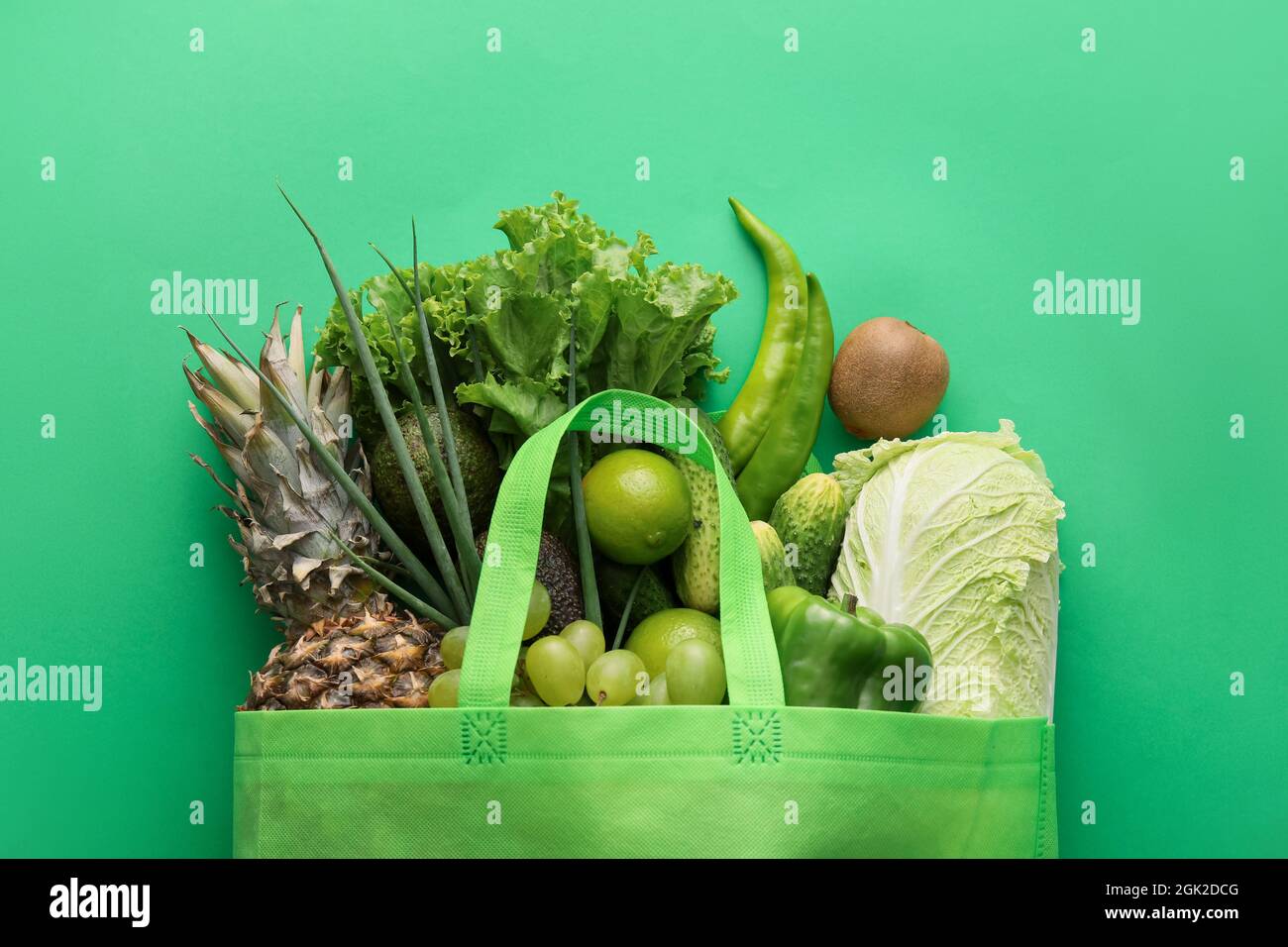 Eco bag with different fruits and vegetables on green background ...