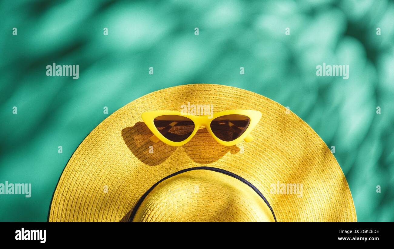 Yellow straw hat and sunglasses over green turquoise background with sunlight and tree shadow ,Minimal summer beach sea Stock Photo