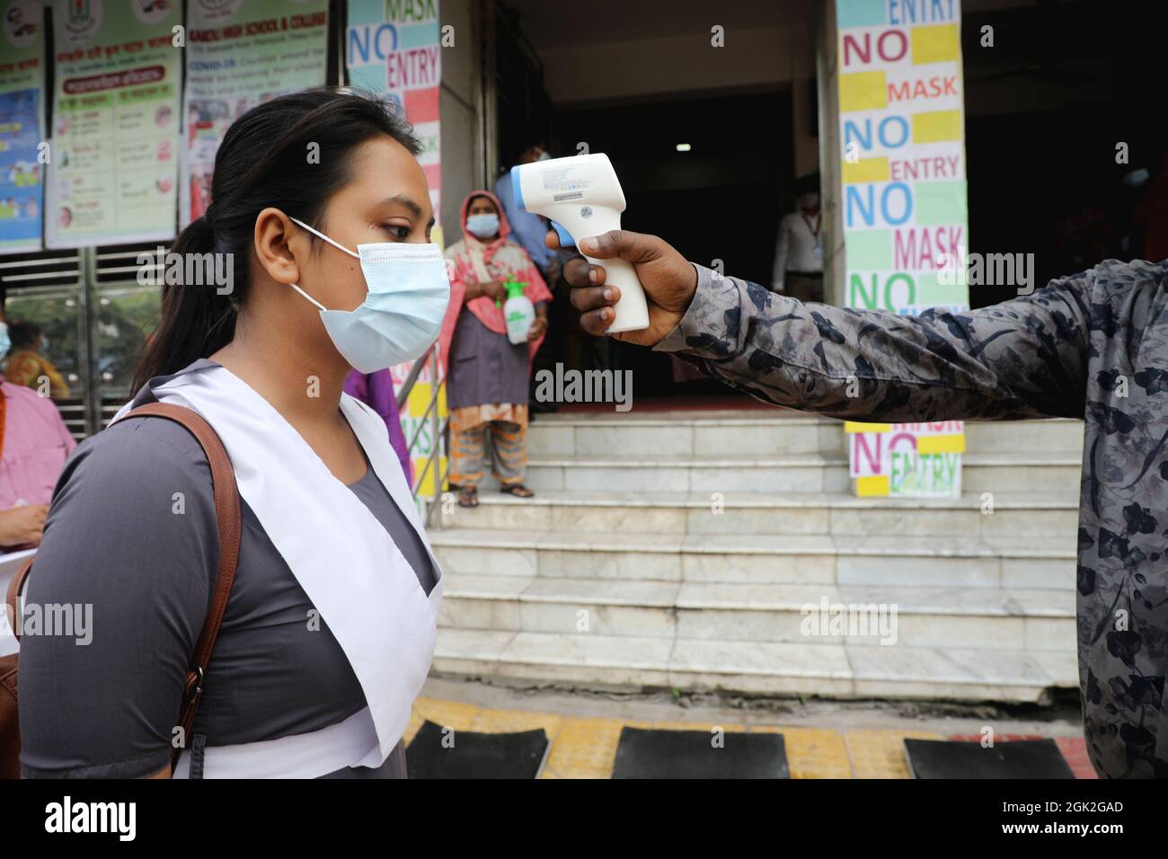 Non Exclusive: A Student of Kakli High School wears face mask  while a person check her the temperature before entering  as protective measures   duri Stock Photo