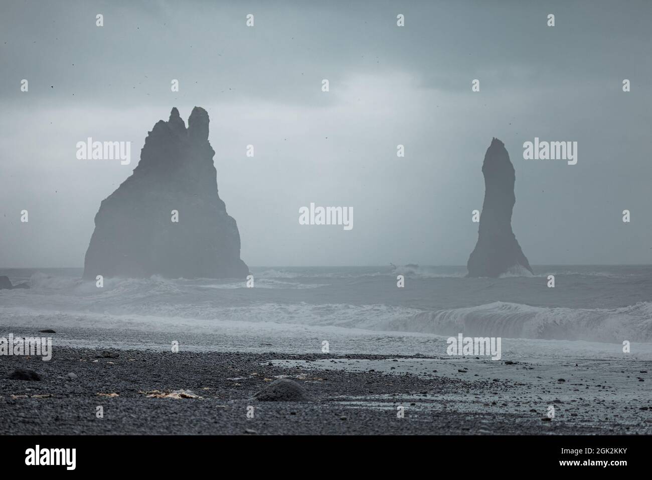 Reynisfjara beach in Iceland with big basalt pillars climbing from water and rocky beach. Cold windi place at the beach with big waves. Stock Photo