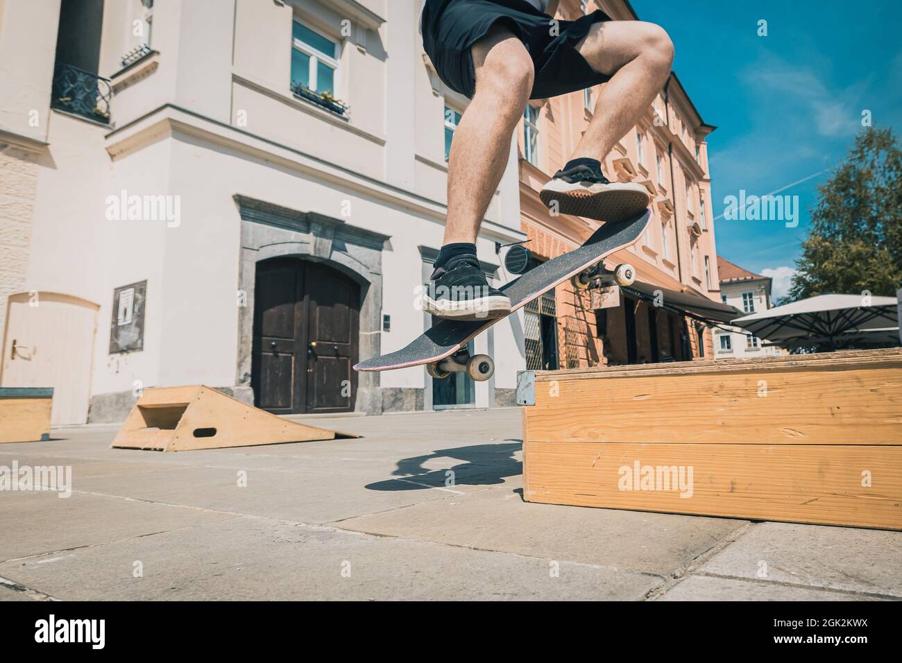 Anonymous skateboarder performing a trick on a wooden box on a sunny day in the city center. Young skater jumping. Stock Photo