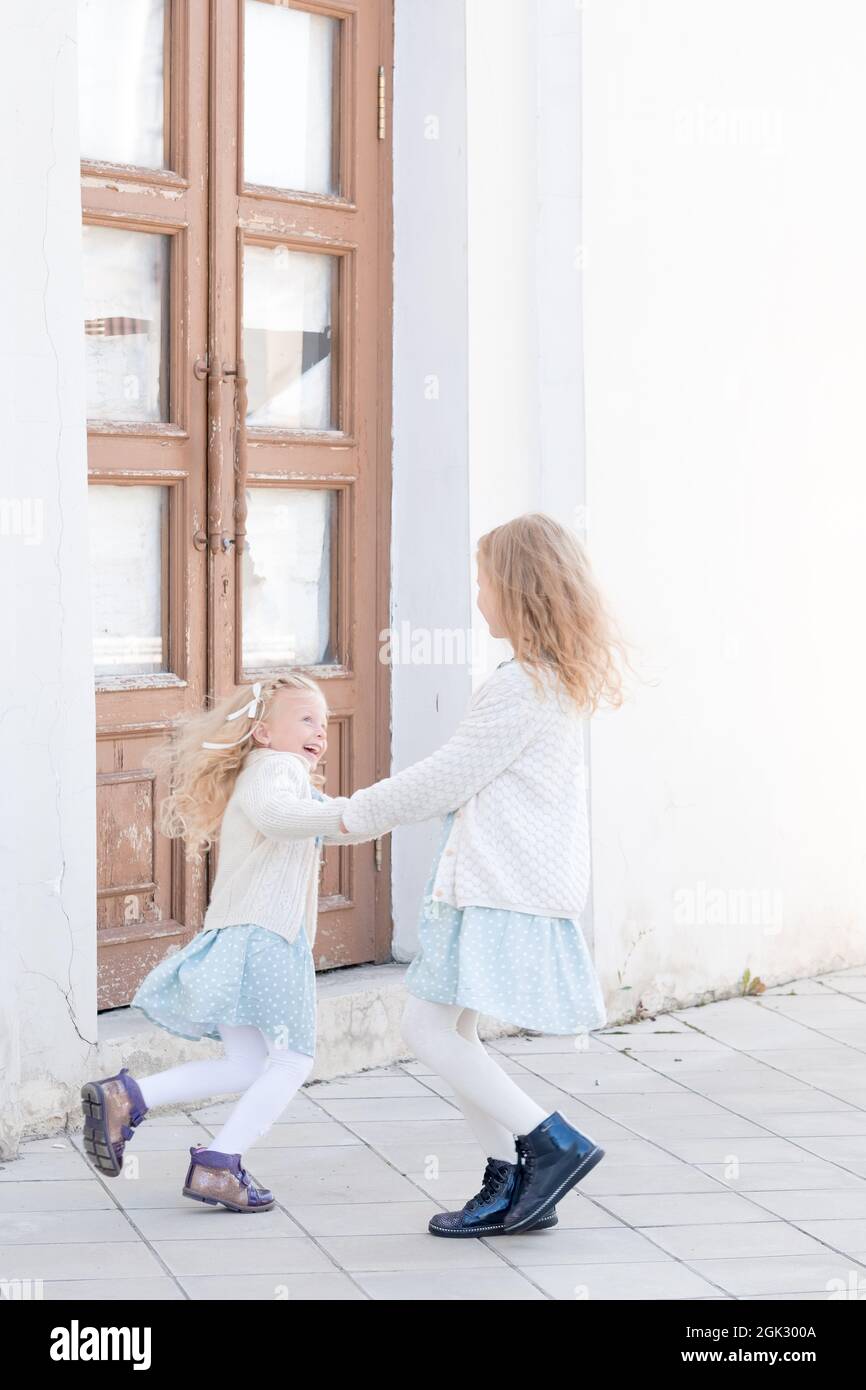 Happy Children Holding Hands. Two Little Girls Enjoying Life Whirl Outdoor Under Sunlight. Happy childhood of two sisters. Walking by the old mansion. Stock Photo