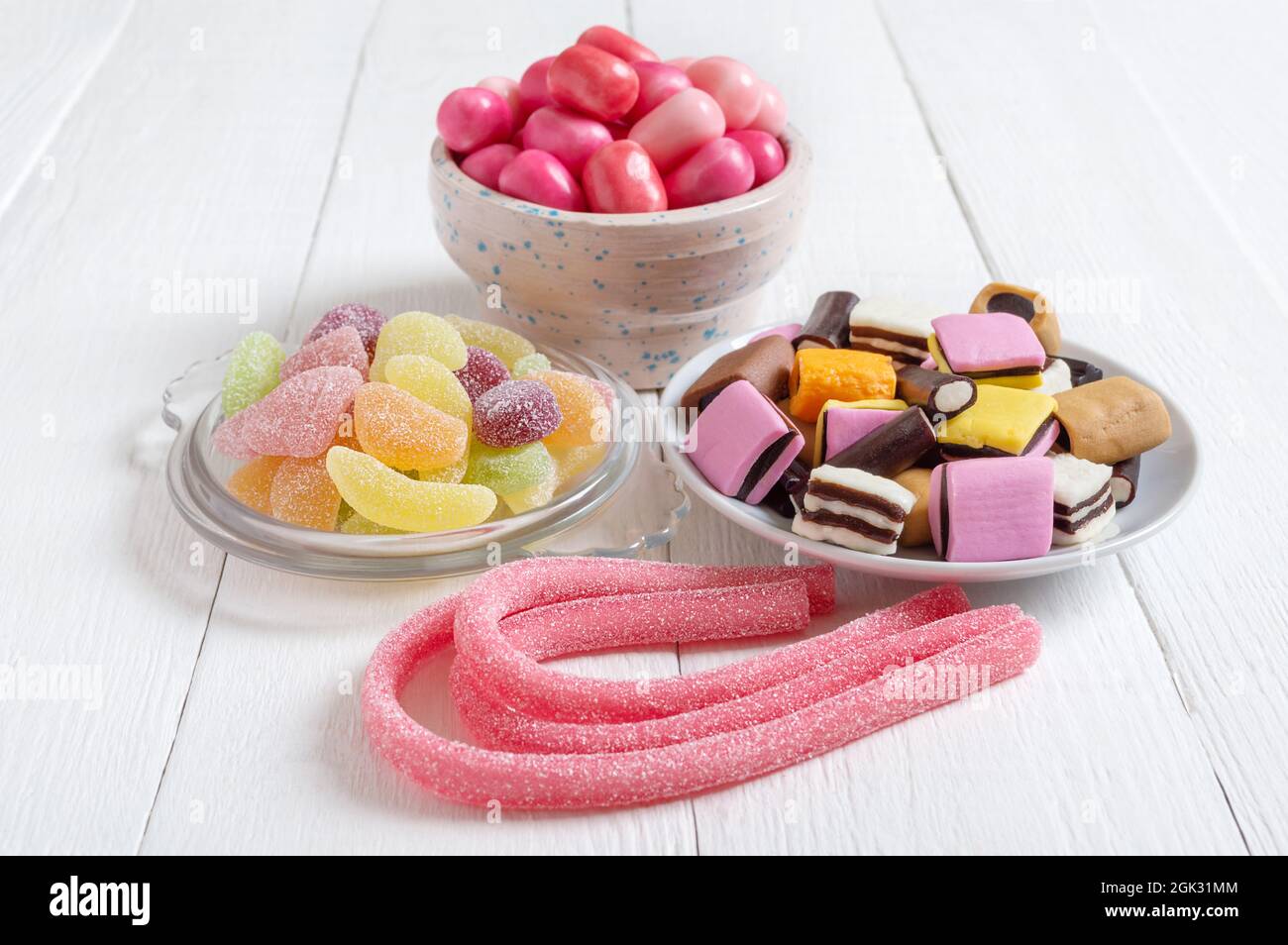 Chewy gummies, liquorice candies, fruit gum in bowls on a white wooden