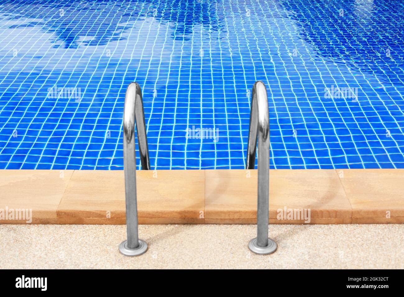 Swimming pool entrance stair closeup, metal grab bar ladder, swimming pool wooden deck edge, poolside blue water background, sea beach summer holidays Stock Photo