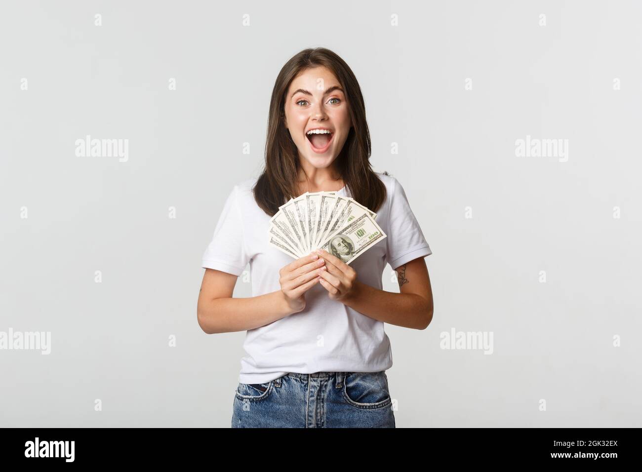 Happy attractive brunette girl holding money and smiling excited, white ...