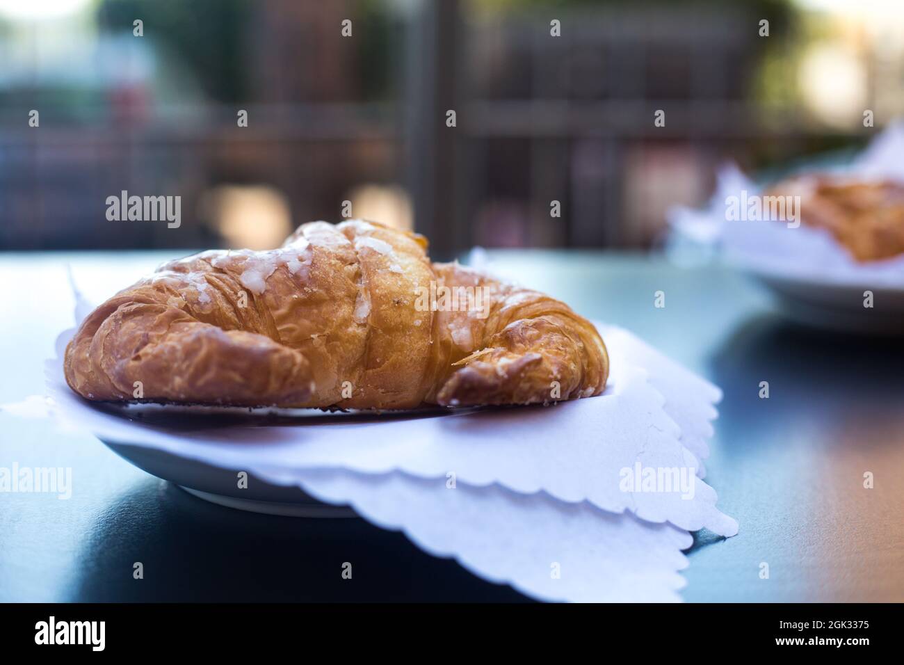 Italian breakfast. Fresh crunchy croissant or cornetto served in outdoor terrace on white napkins with view to neighbour house in background. Summer Stock Photo