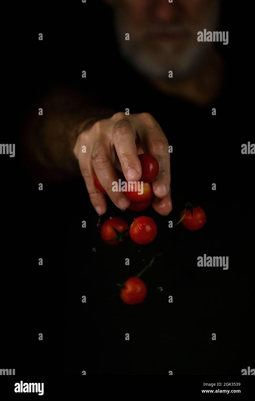 Hand dropping cherry tomatoes against black background Stock Photo