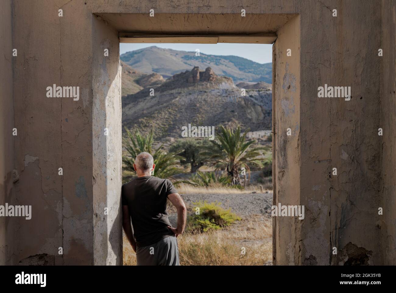 Rear view of adult man standing in doorway of an abandoned house looking at view Stock Photo