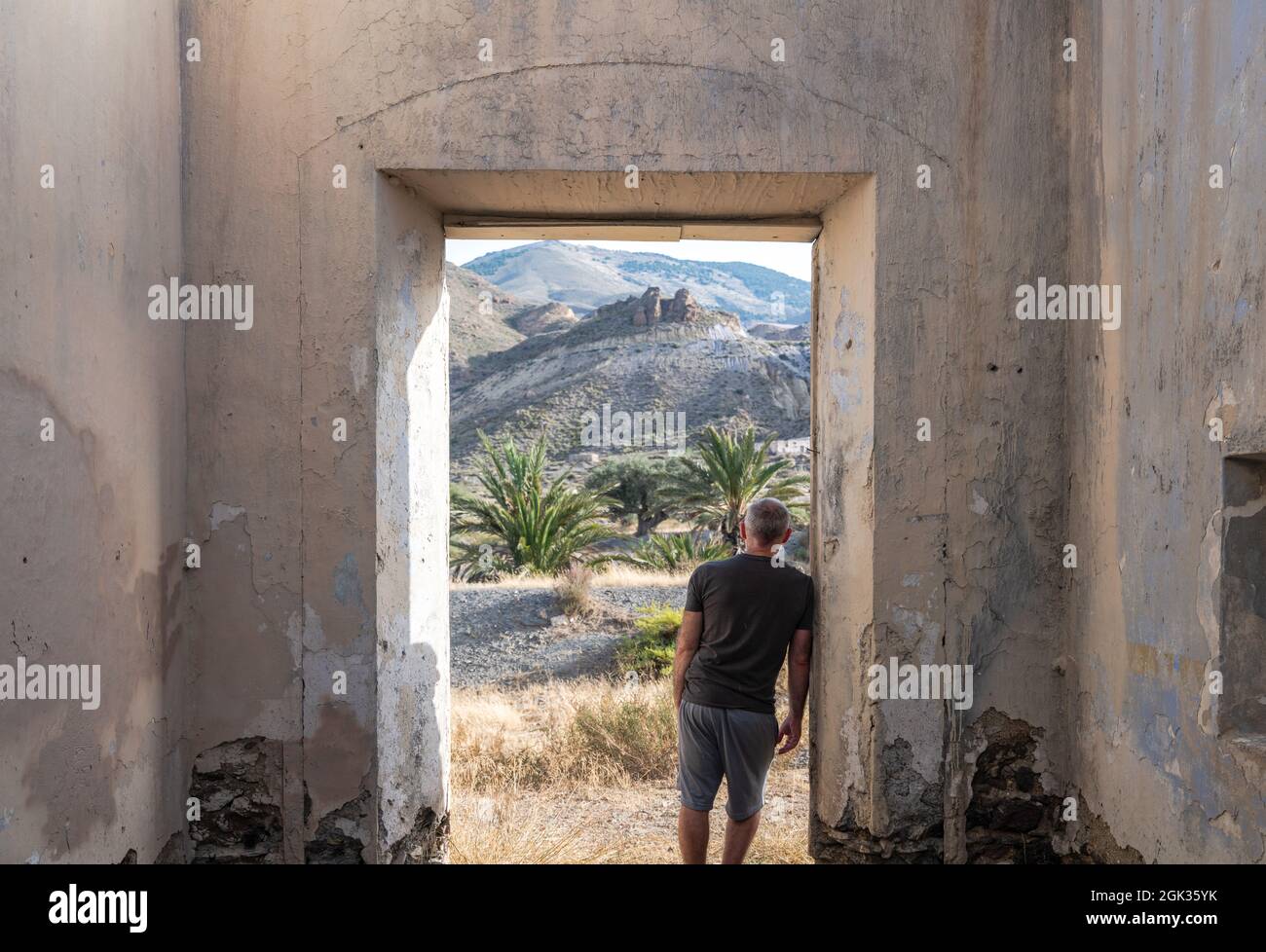 Rear view of adult man standing in doorway of an abandoned house looking at view Stock Photo