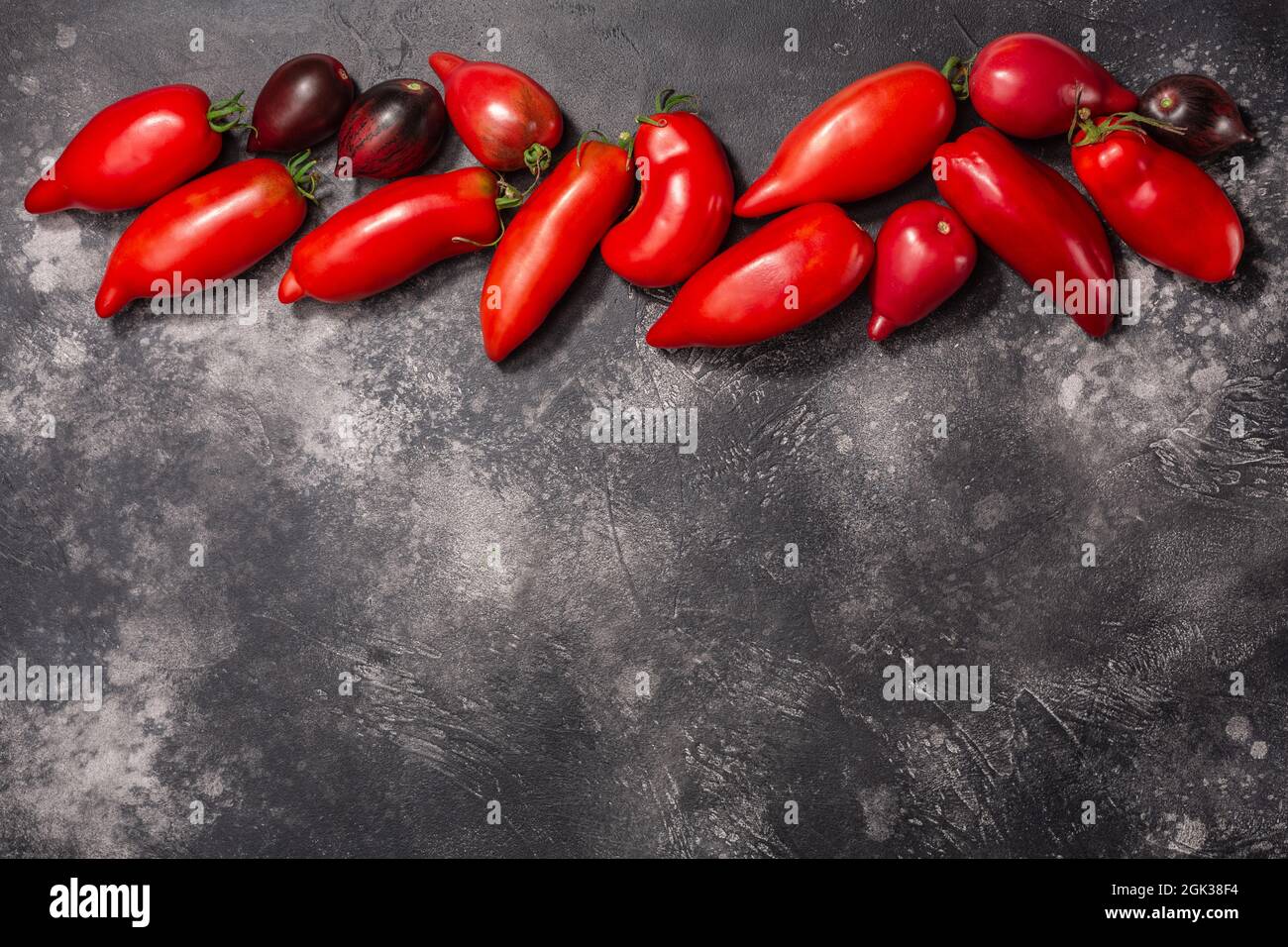 Ripe pepperlike heirloom tomatoes atop dark textured backdrop, copy spce, top view (Solanum lycopersicum fruits) Stock Photo