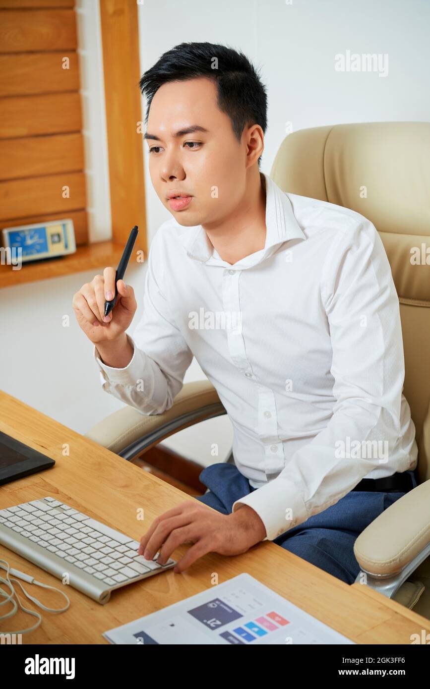 Pensive young UX designer working on computer at his office desk and creating new design Stock Photo