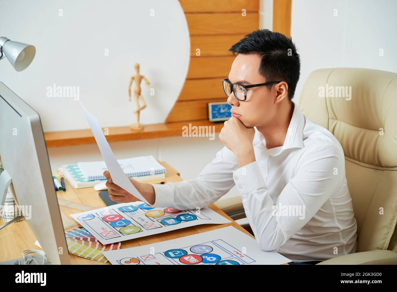 Pensive young UX designer reading document with requirement specification for new project Stock Photo