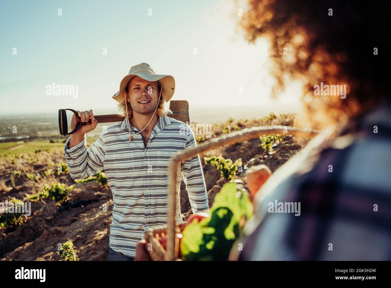 Caucasian male farm worker holding shovel talking to female co worker standing on farmlands  Stock Photo