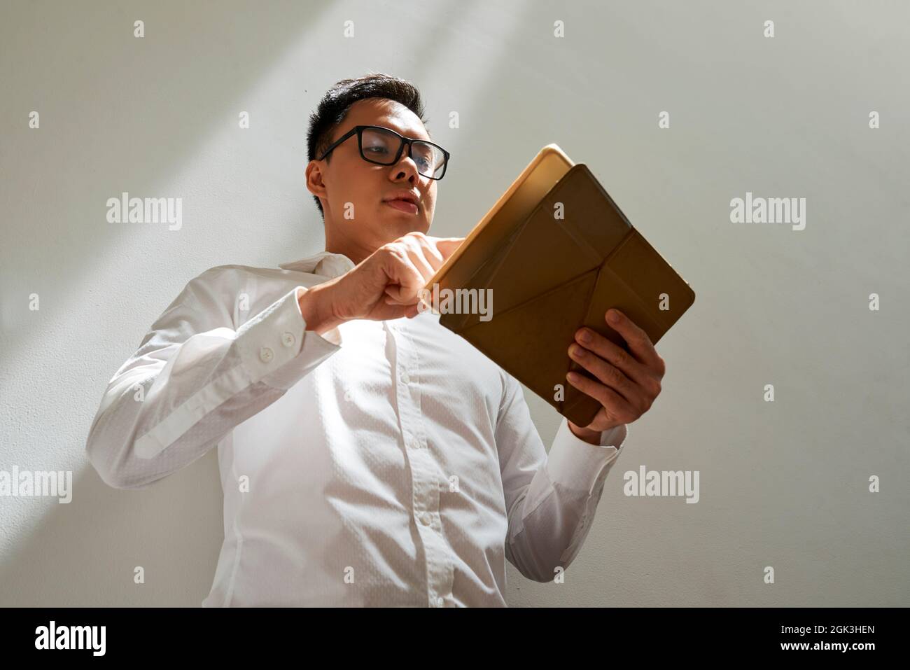 Businessman in white shirt and glasses checking document or e-mail on tablet computer, view from below Stock Photo