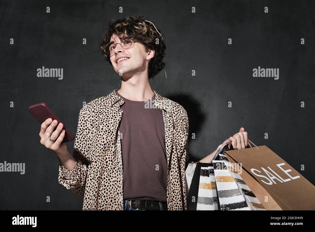 Young man with shopping bags using mobile phone for online shopping isolated on black background Stock Photo