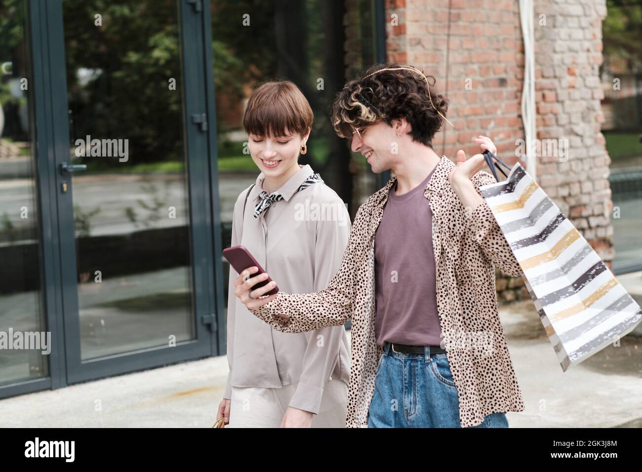 Young man showing new collection on the mobile phone to his girlfriend while they shopping together outdoors Stock Photo