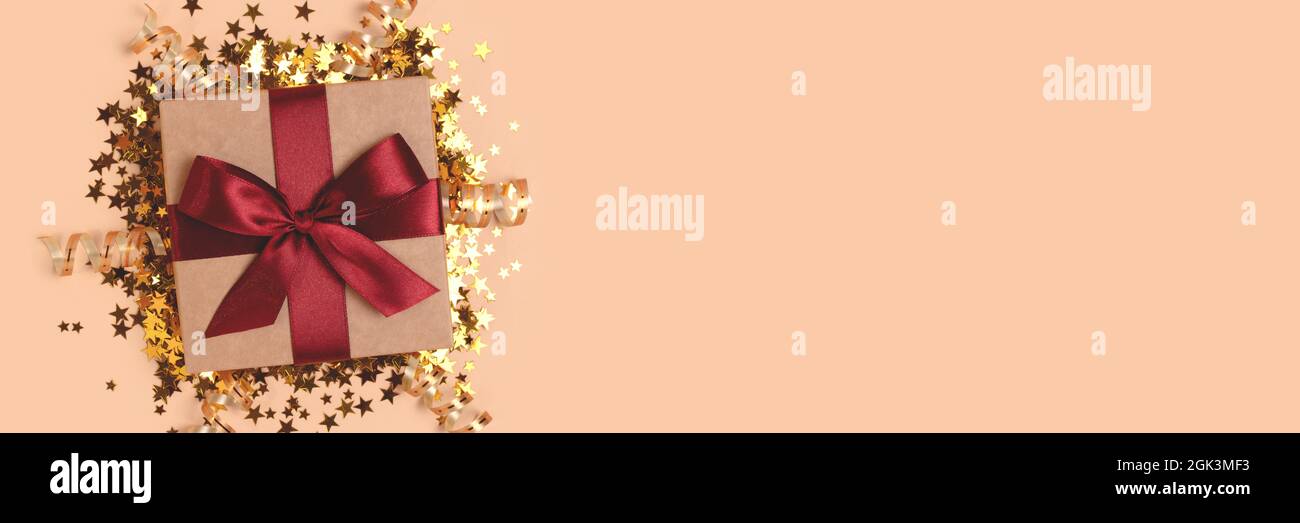 Banner with gift box with red ribbon and gold confetti on a beige background. Stock Photo