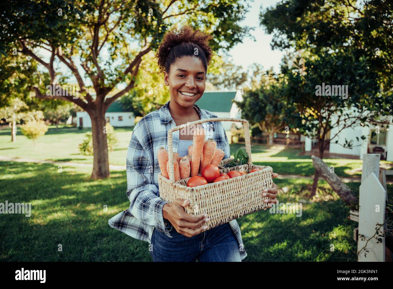 Mixed race female walking through farm village smiling looking happy after picking fresh vegetables from garden  Stock Photo