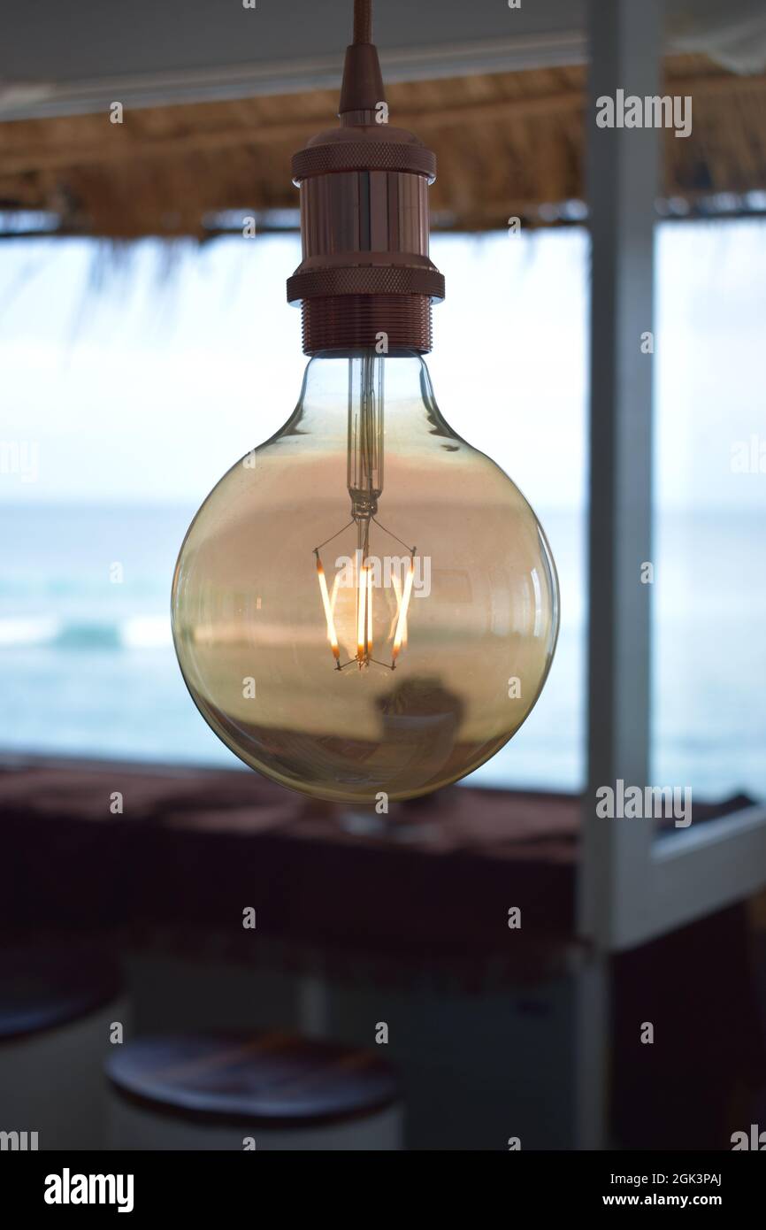 Transparent vintage light bulb with glowing filaments and beach in the background Stock Photo