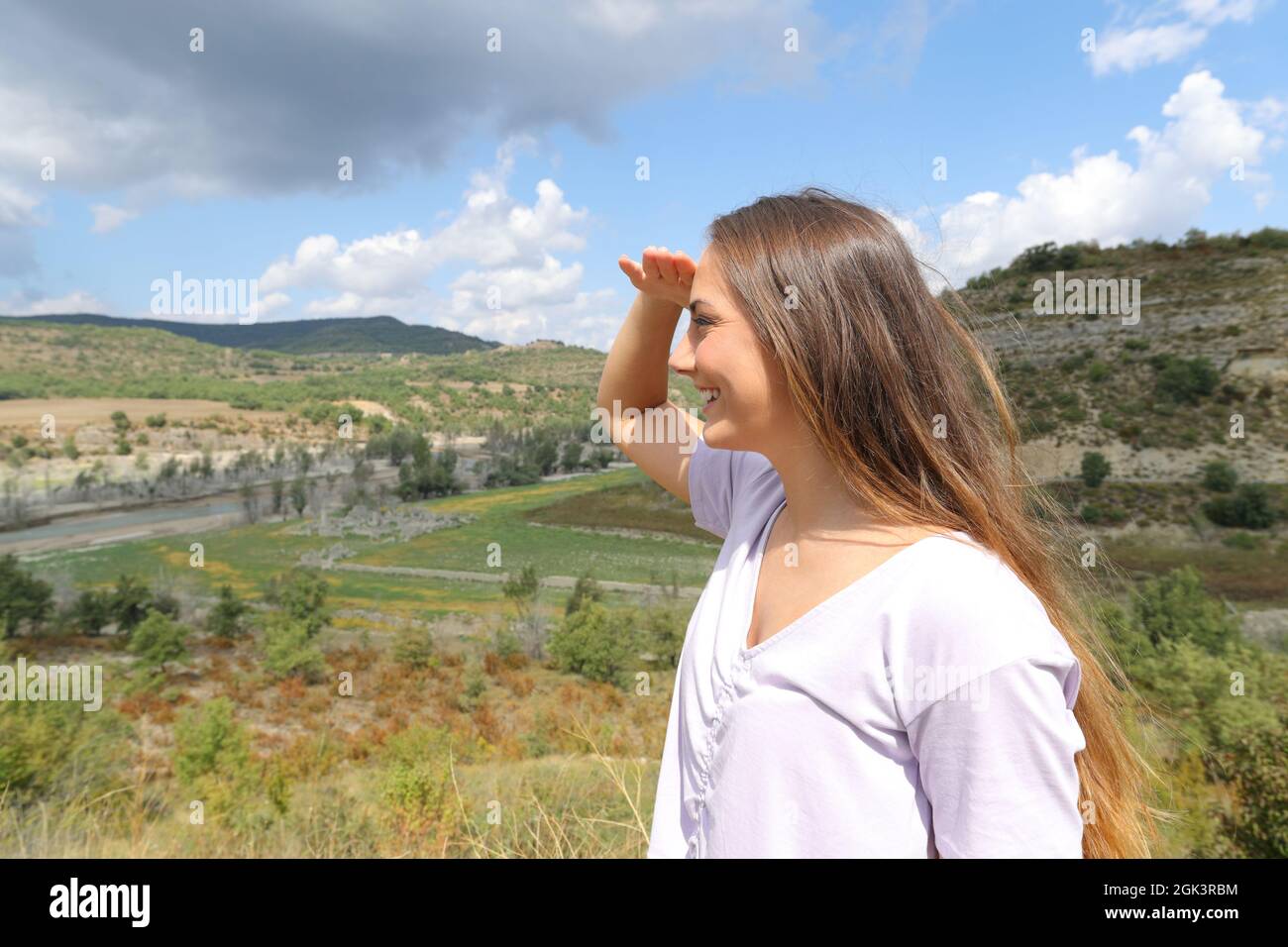 Happy woman looking away protecting from sun with her hand in the mountain Stock Photo