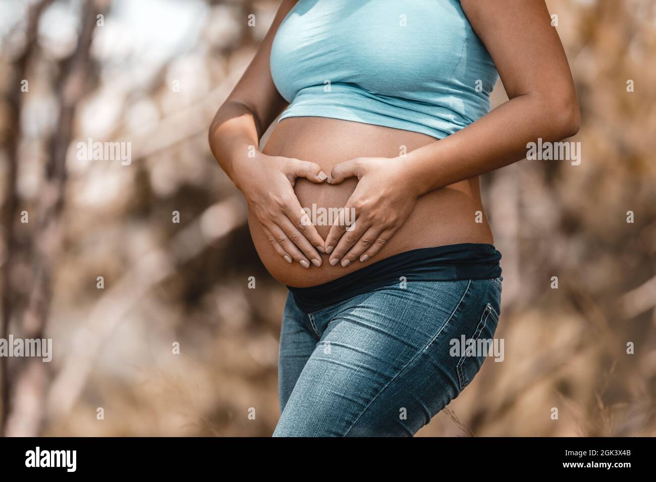Tummy of a Pregnant Woman. Making Heart Shape by her Hands on Belly. Body Part. Enjoying Pregnancy. Young Happy Family. Stock Photo