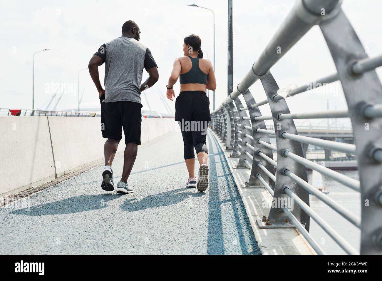 Rear view of sportive couple in sports clothing running together along the bridge in the morning Stock Photo