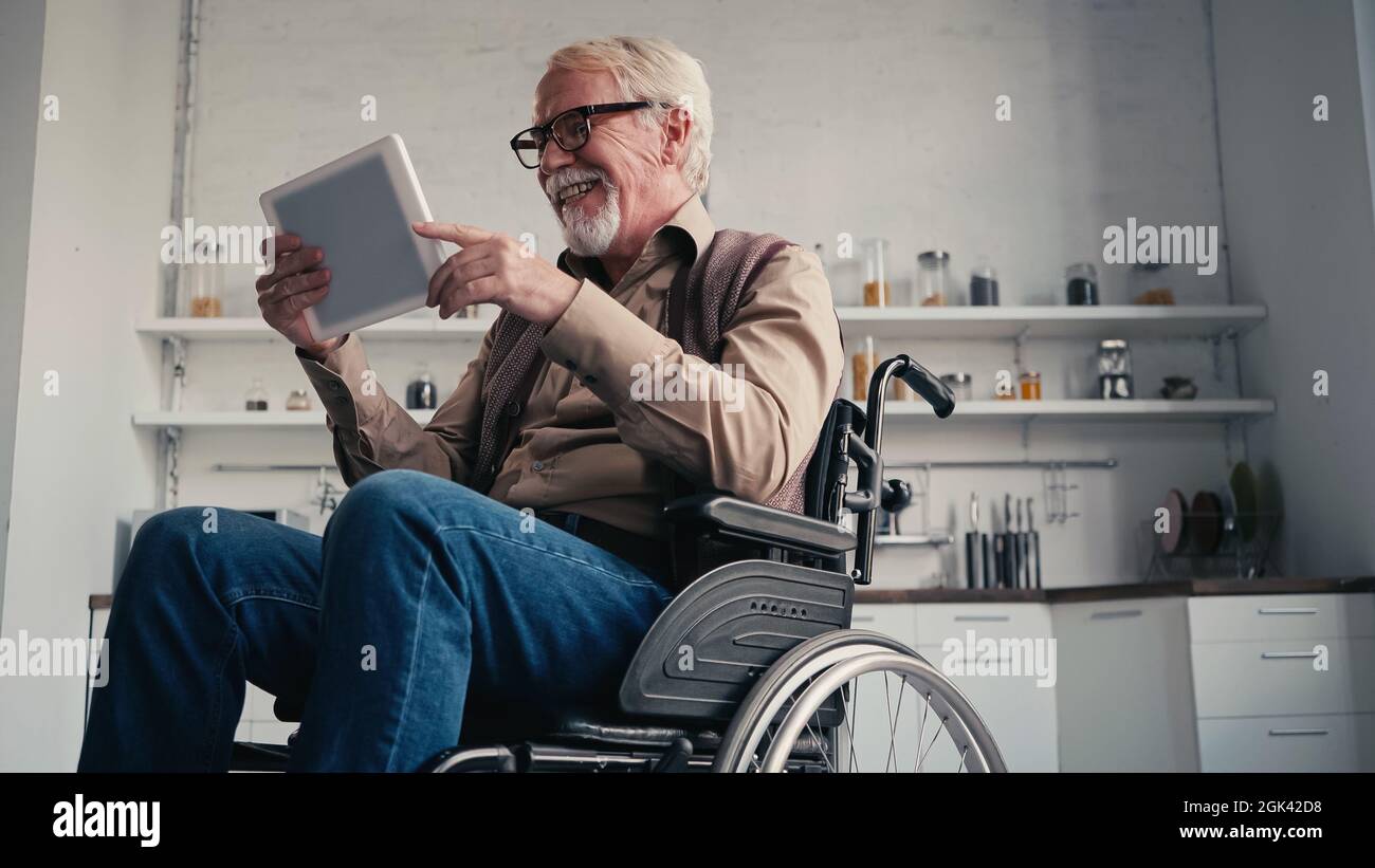 Smiling disabled pensioner in wheelchair using digital tablet at home Stock Photo