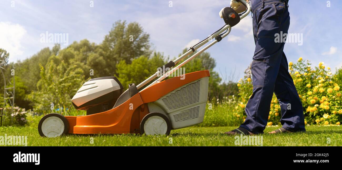 A professional gardener with a lawnmower cares for the grass in the backyard. Stock Photo