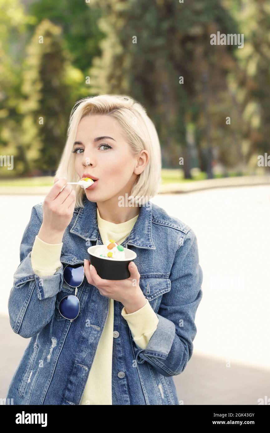 Beautiful young girl eating tasty yogurt ice cream outdoors Stock Photo
