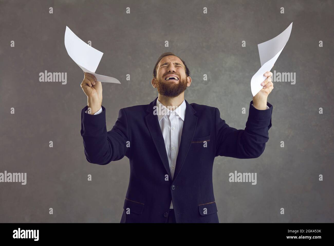 Young man holding sheets of paper and crying stressed with office job and business paperwork Stock Photo