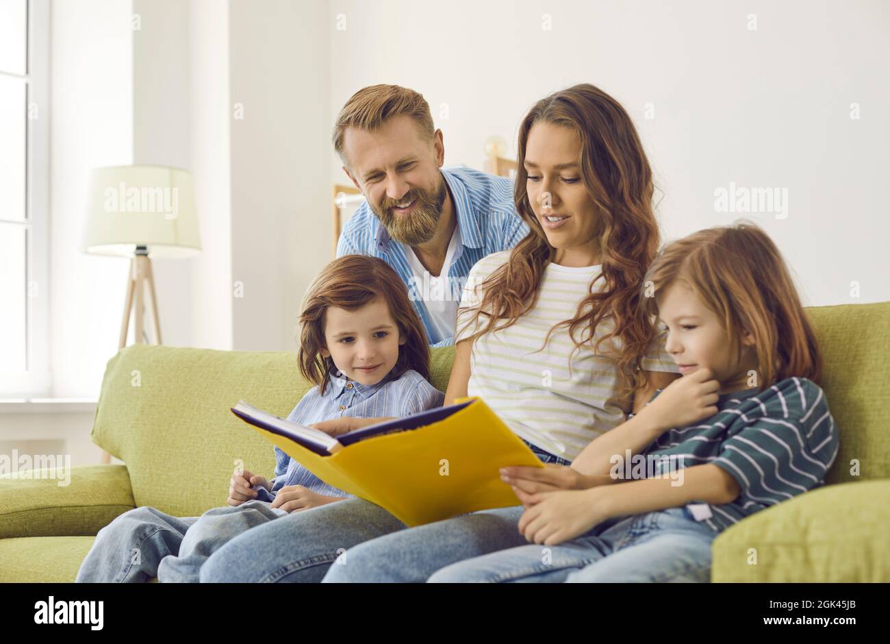 Happy family sitting on couch at home, looking through photo album or reading book Stock Photo