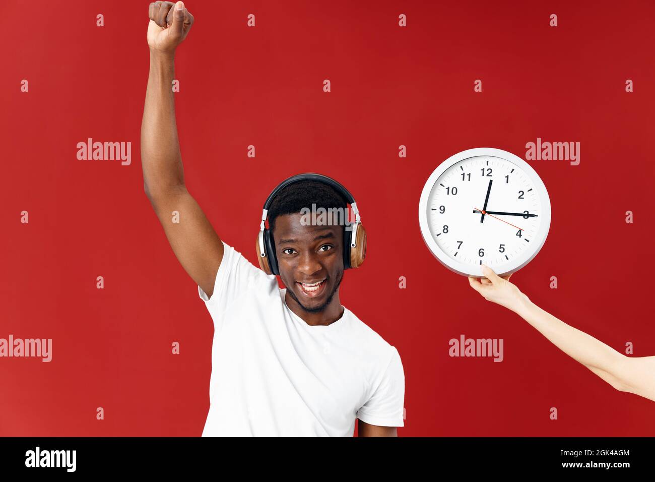 cheerful man in headphones listens to music next to the clock hand above his head Stock Photo