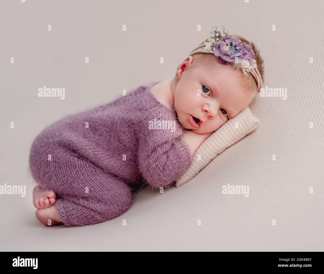 Awake newborn girl with flower diadem lying on tiny pillow Stock Photo