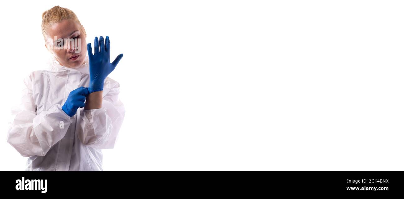 A woman puts on latex gloves in a chemical protection suit. Isolated on white background. Stock Photo