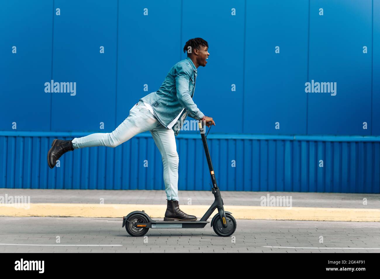 modern african american on electric scooter, business man is one to work, student is one to study, against the background of a blue building, side vie Stock Photo