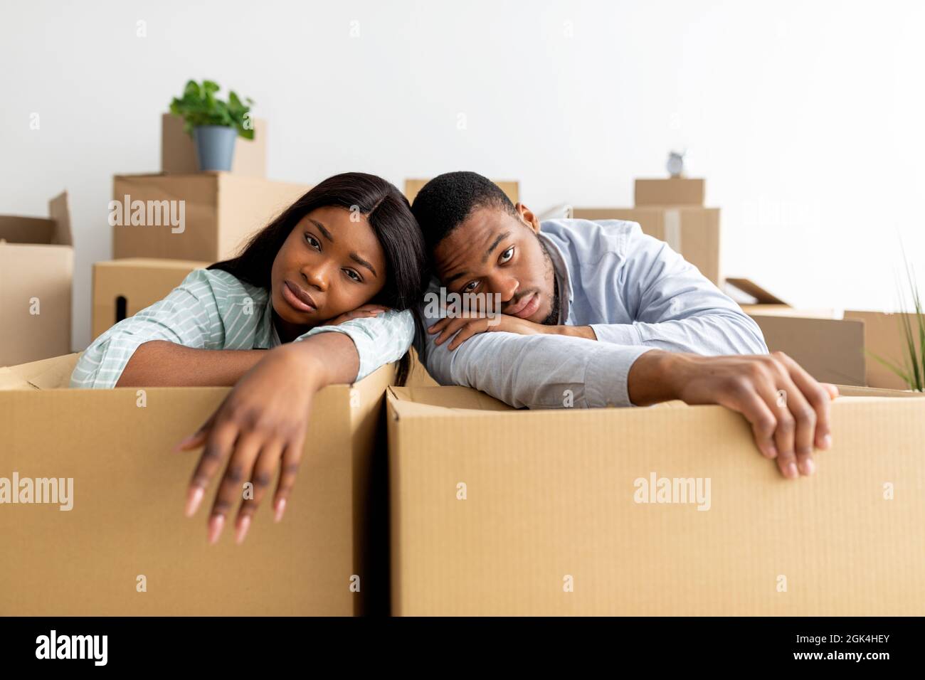 Moving stress concept. Exhausted black family leaning on unpacked boxes ...
