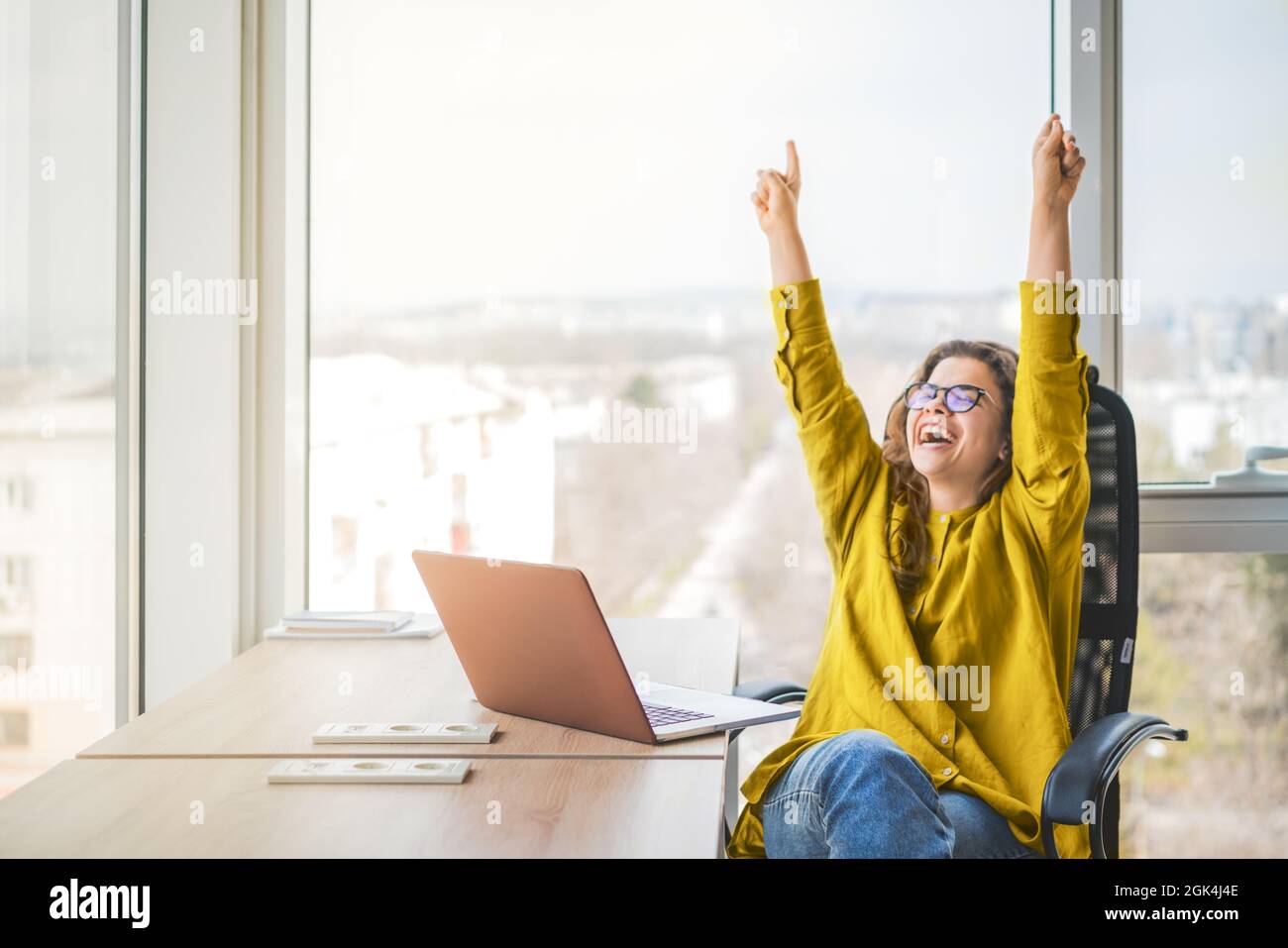 Happy successful businesswoman in yellow shirt raising fists with ambition. Women going up career ladder. Business achievement and promotion concept Stock Photo