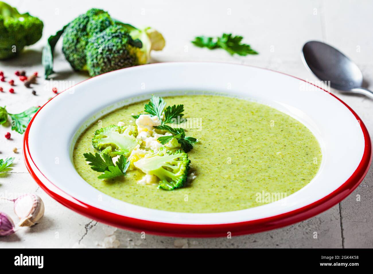 Broccoli soup puree with feta cheese in plate on gray tile background with ingredients. Cooking healthy food concept. Stock Photo