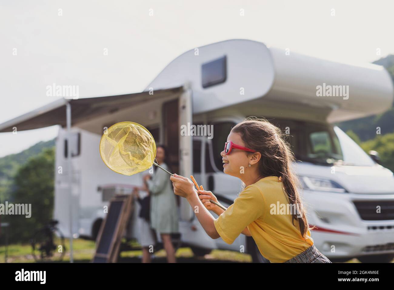 Happy small girl standing outdoors with butterfly net by caravan car, family holiday trip. Stock Photo