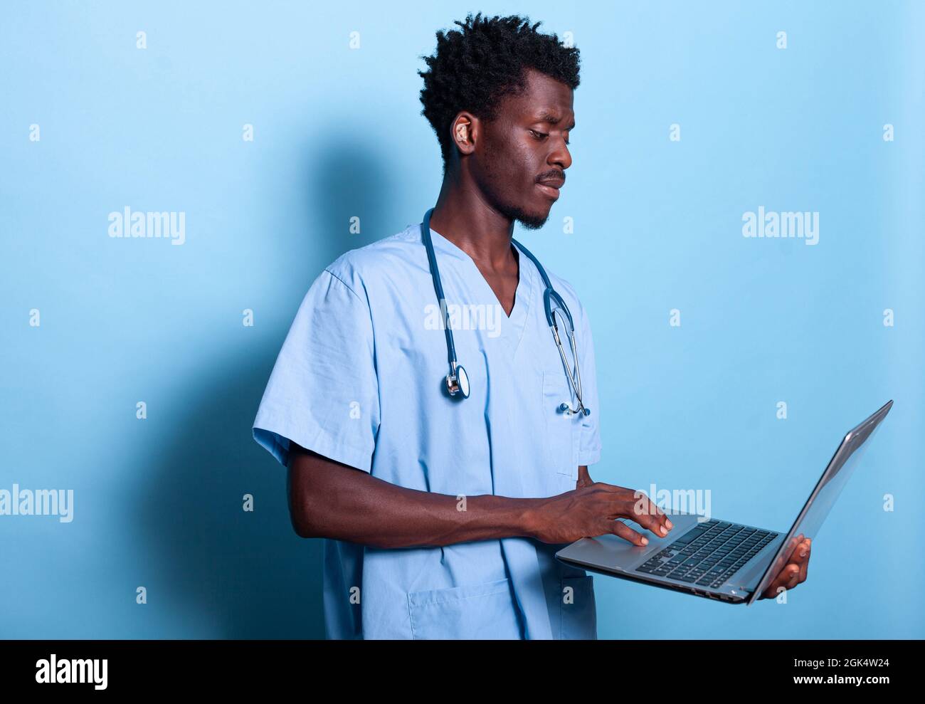 African american man nurse looking at laptop in hand. Black medical  assistant with blue uniform and stethoscope holding modern device, standing  over isolated background. Healthcare specialist Stock Photo - Alamy