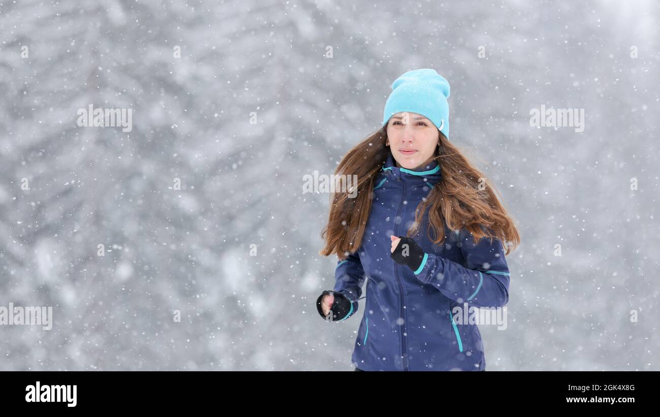 Young pretty woman jogging in winter park. Outdoors cold weather running lifestyle background with copy space. Stock Photo