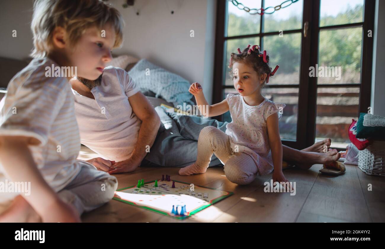 Unrecognizable father with two small children resting indoors at home, playing board game. Stock Photo