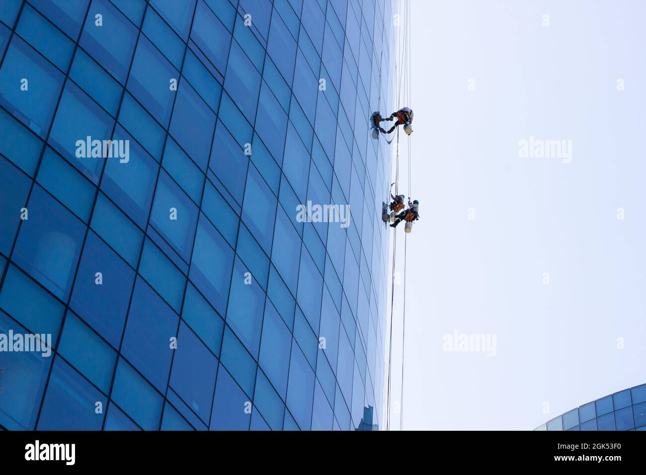 Window cleaning workers hanging outside blue glass office building. Risky job, dangerous work