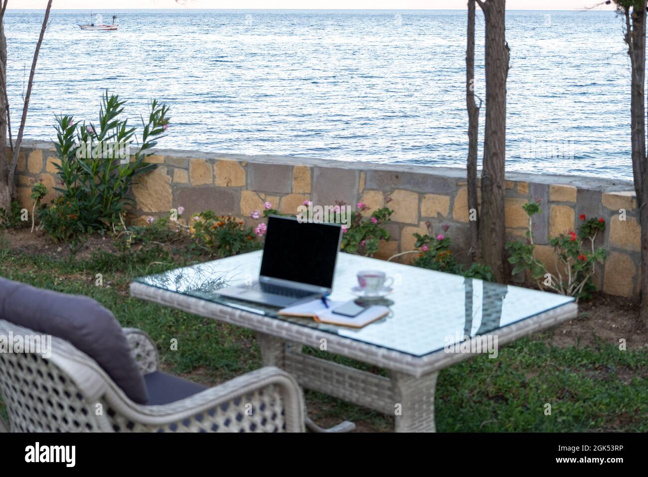 working from summer house remote concept in pandemic, table ready for work with laptop notebook pen phone near the seaside Stock Photo