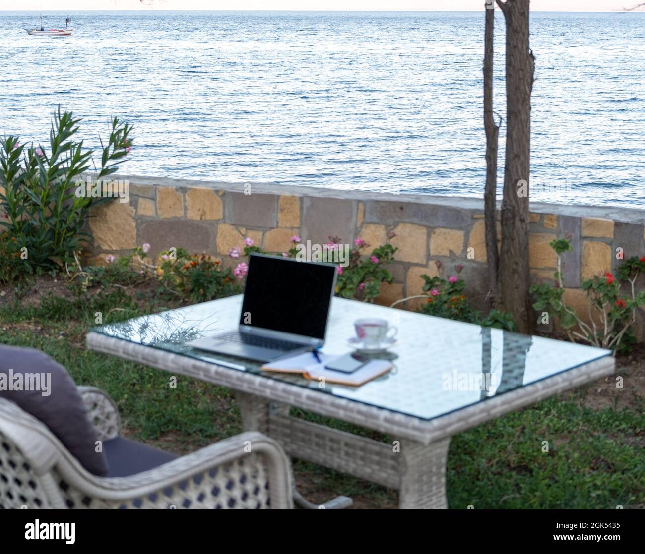 working from summer house remote concept in pandemic, table ready for work with laptop notebook pen phone near the seaside Stock Photo