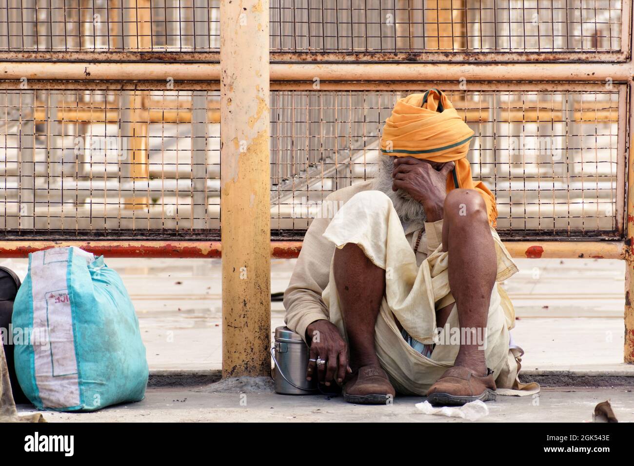 Orchha, Madhya Pradesh, India - March 2019: An aged Indian man wearing an orange turban sitting sad and worried outside the fences of a Hindu temple i Stock Photo