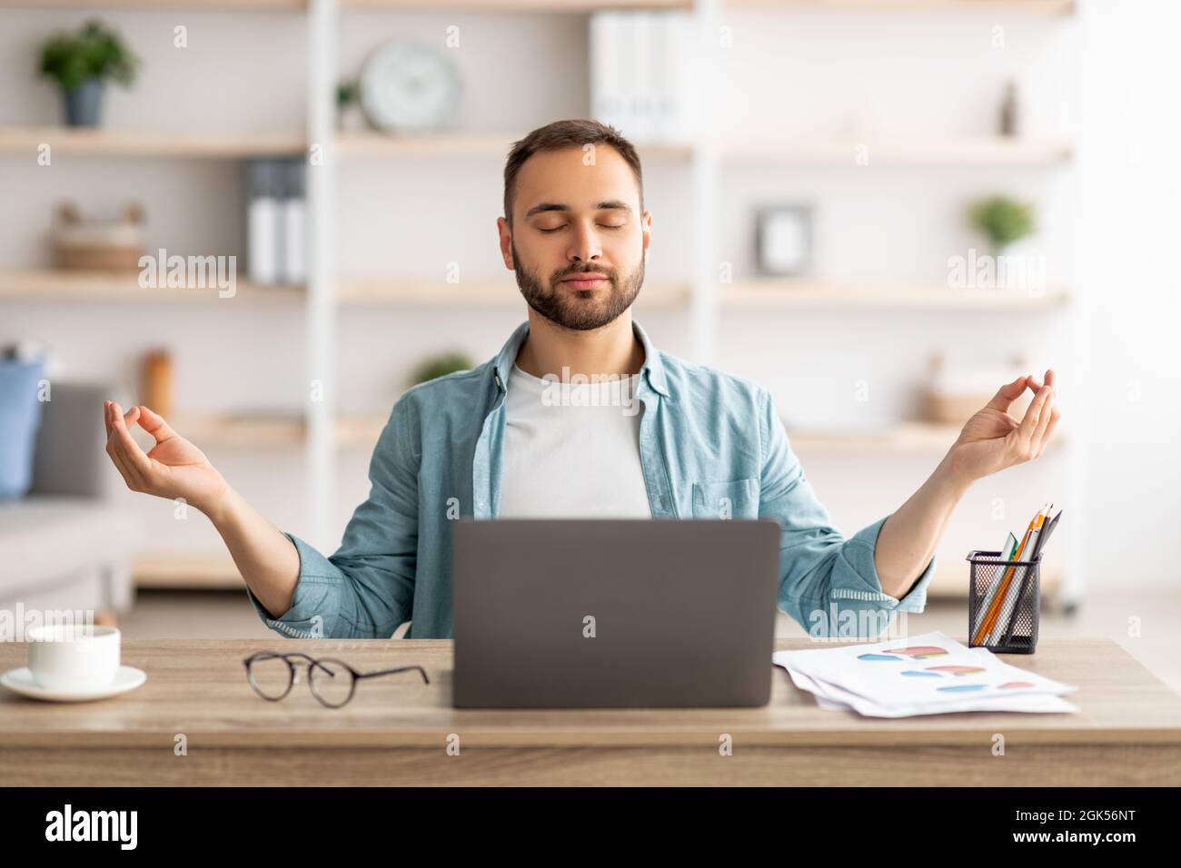 Workplace stress management. Calm Caucasian man meditating with closed eyes in front of laptop pc at home office Stock Photo