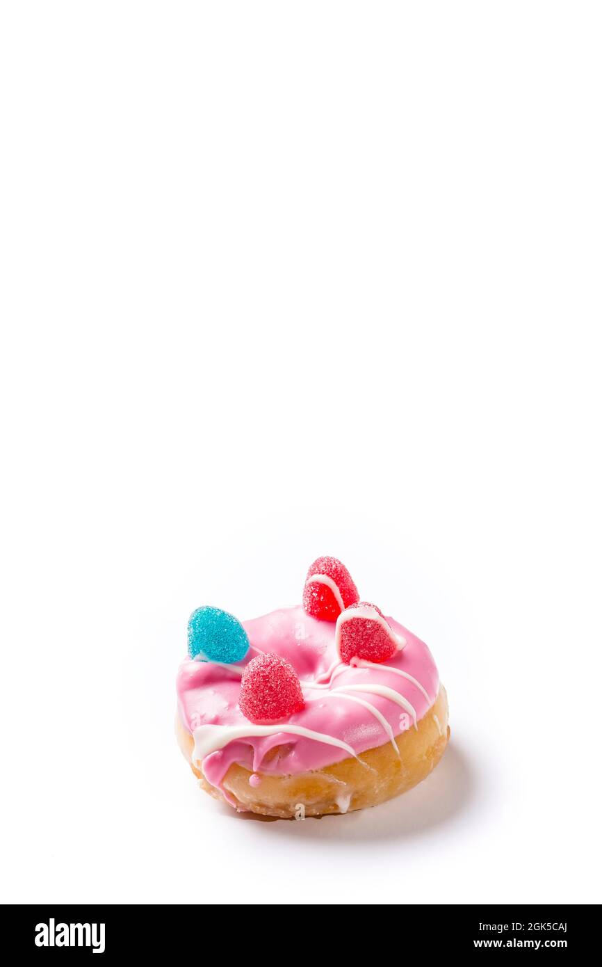 Photograph of a pink donuts painted with white chocolate and decorated with jelly beans.The photo is taken in vertical format on a white background an Stock Photo