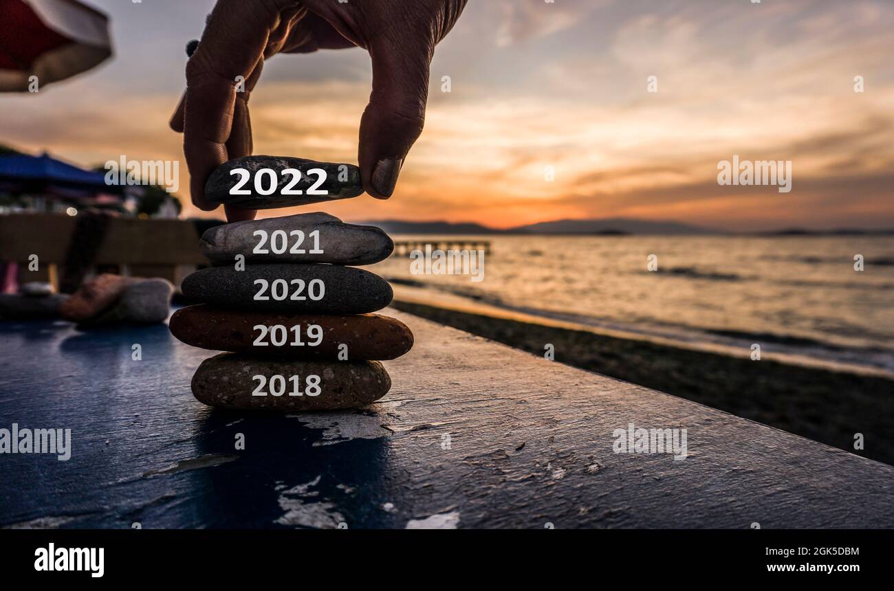 New Year 2022 is coming concept. Old year 2021 change to 2022. Happy new year concept. New hopes and excitements. Man adding stone to pebble tower. Stock Photo